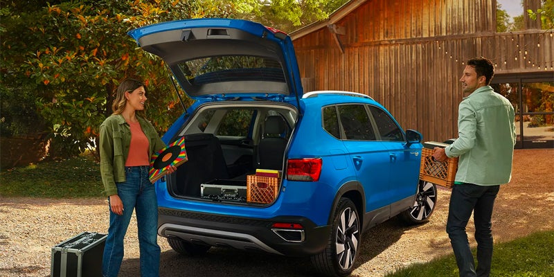 A blue 2024 Volkswagen Toas with the trunk open and a man and woman unloading the vehicle on a sunny day